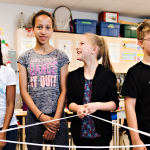 Youth stand in a semi-circle holding a web of yarn, smiling.