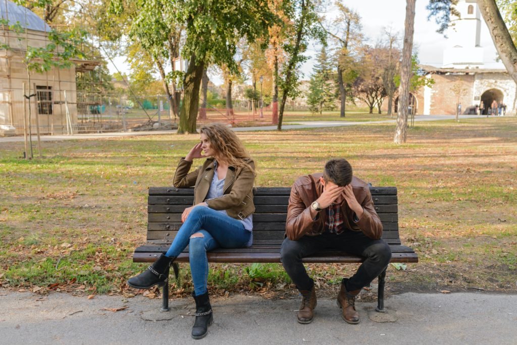 Two people sitting on a park bench, distraught.