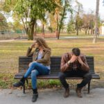 Two people sitting on a park bench, distraught.