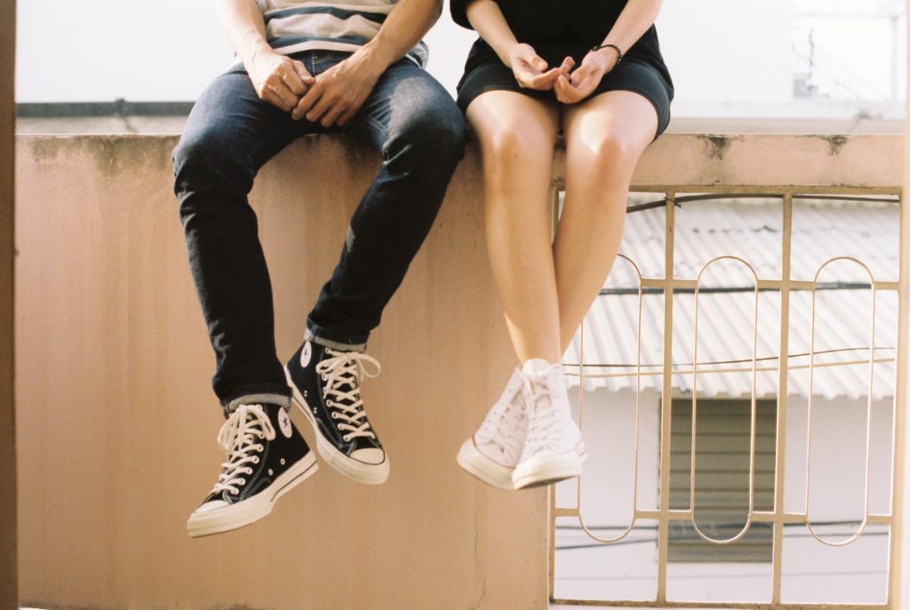 two teens sitting on a bench, legs dangling off the edge