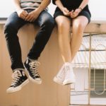 two teens sitting on a bench, legs dangling off the edge