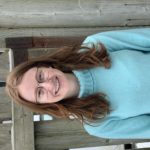 Haley Bauman wearing bright blue turtleneck sweater standing in front of a wood fence.