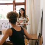 Two young people sit facing a woman who is standing in front of a whiteboard with a marker in hand.