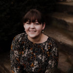 White woman sitting on steps smiling up at the camera, wearing floral top.