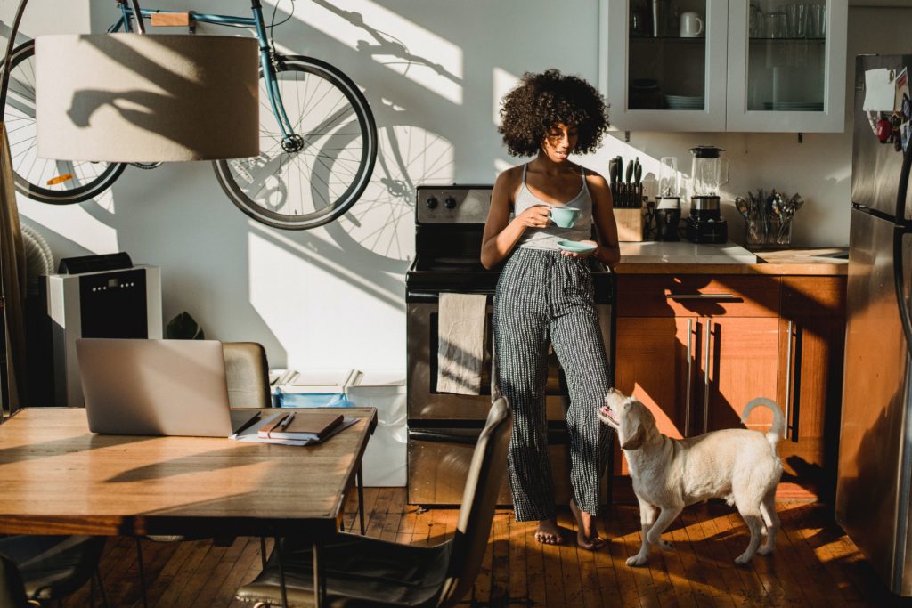 Black woman with coffee near dog standing in kitchen.