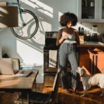 Black woman with coffee near dog standing in kitchen.