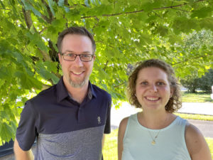 Ben Janzen and Amy Zavitz standing together under a tree on a sunny day.