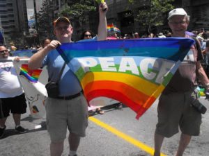 Tim O'Connor holding a rainbow flag that says PEACE at a street march.