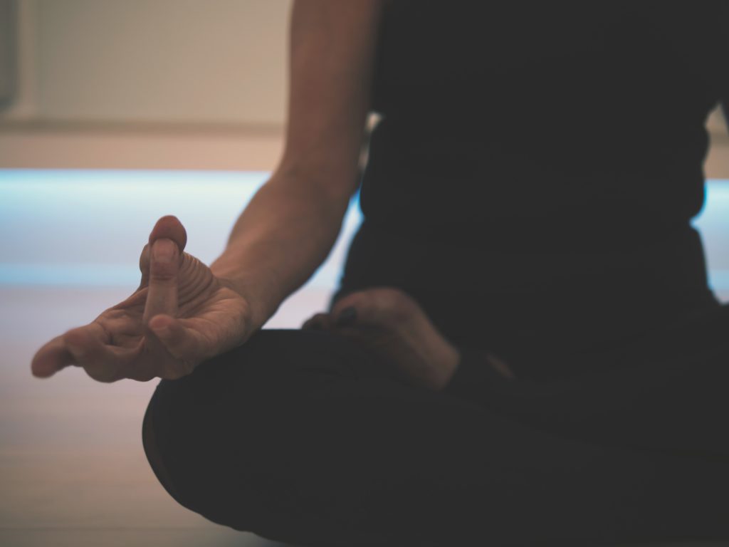 A person is sitting on the floor, crossed legs. They hold their hand meditatively. The photo is cropped to see only the hand and lower part of the body.