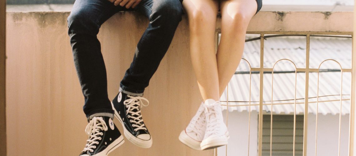 two teens sitting on a bench, legs dangling off the edge